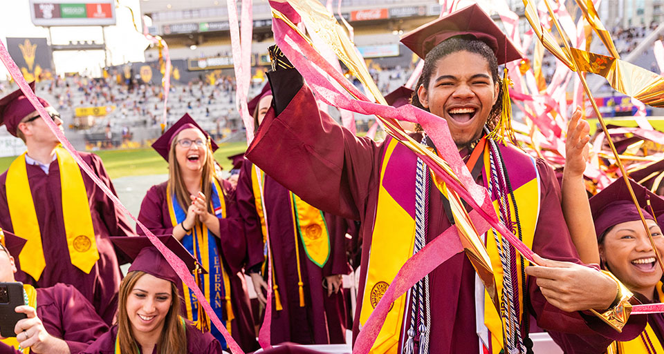 An ASU graduate smiles and celebrates after a graduation ceremony at the ASU football field.