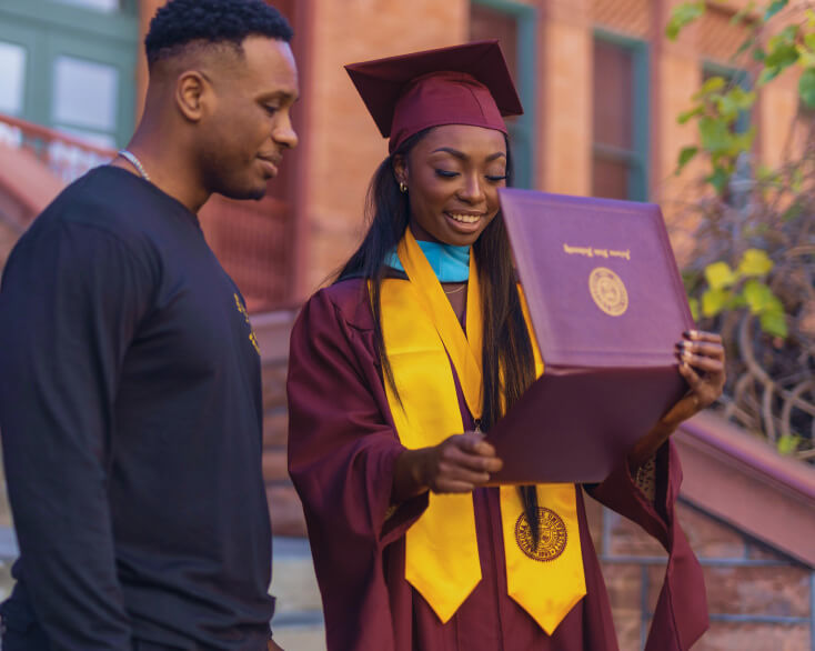 An ASU在线 graduate dressed in a cap and gown admires her diploma.