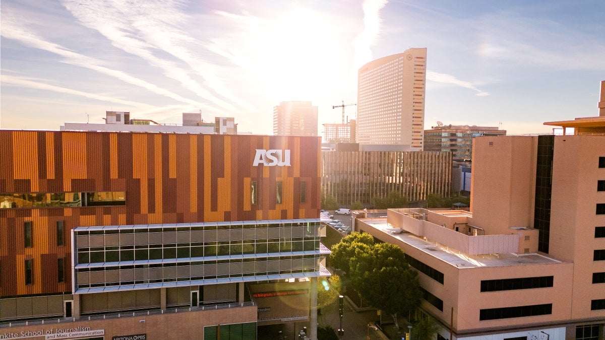 The sun casts rays over the top of an orange and maroon striped building with an ASU sign